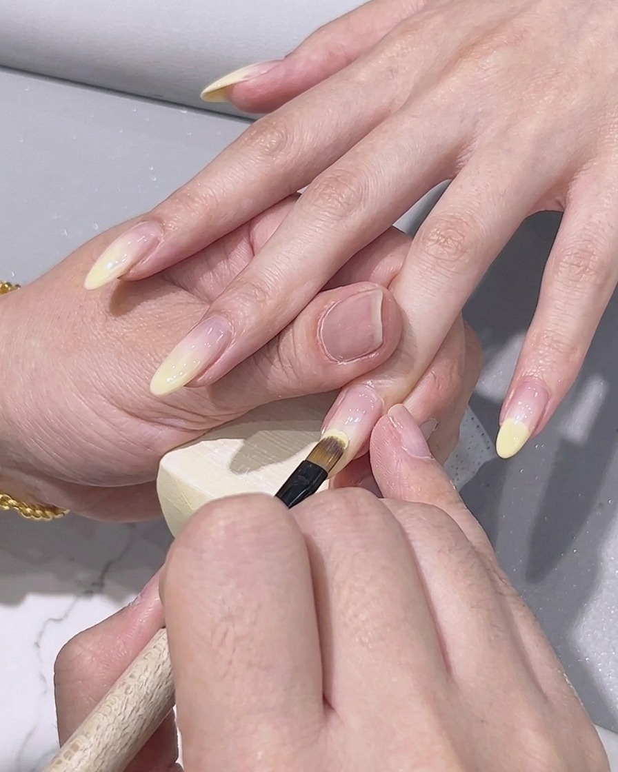 Un pinceau de détail fin appliquant du vernis gel jaune citron sur le bout dun ongle.