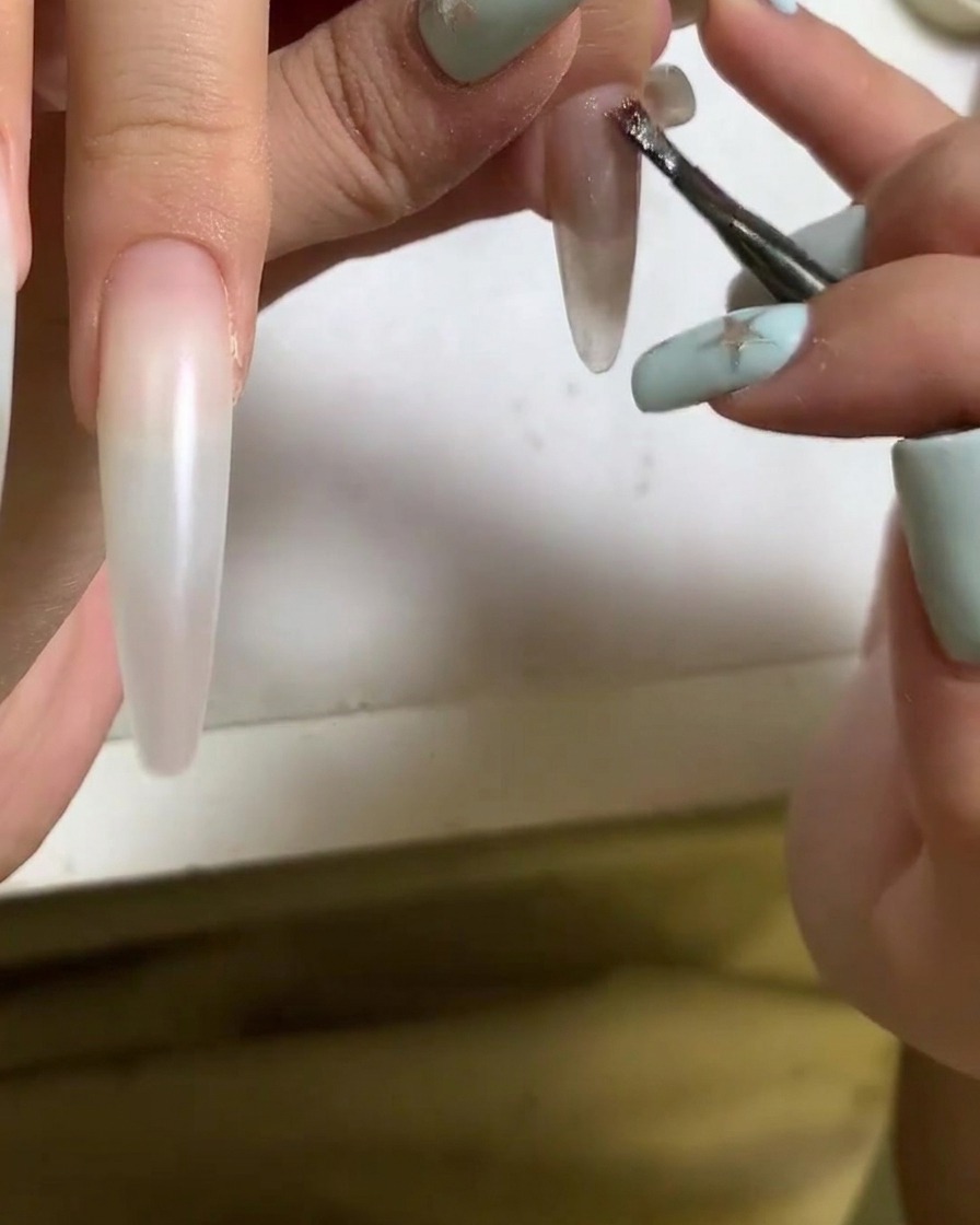 Un pinceau appliquant du vernis gel cat eye sur la surface dun ongle en acrylique.