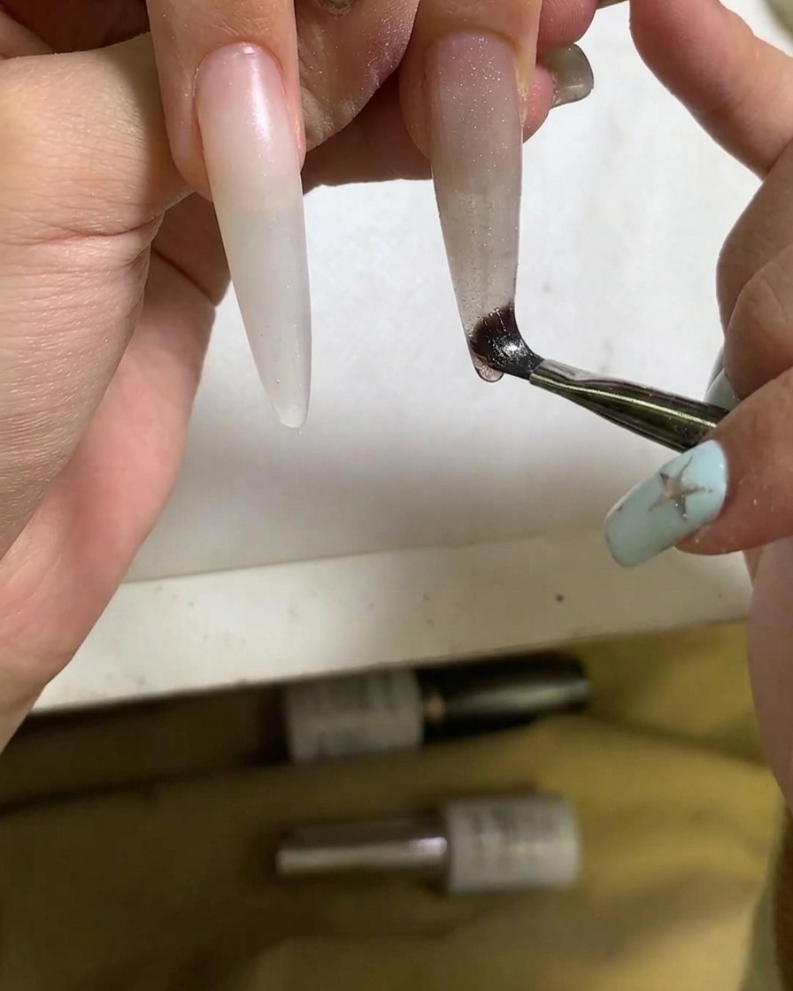 Gros plan dun pinceau appliquant du vernis gel cat eye sur longle.
