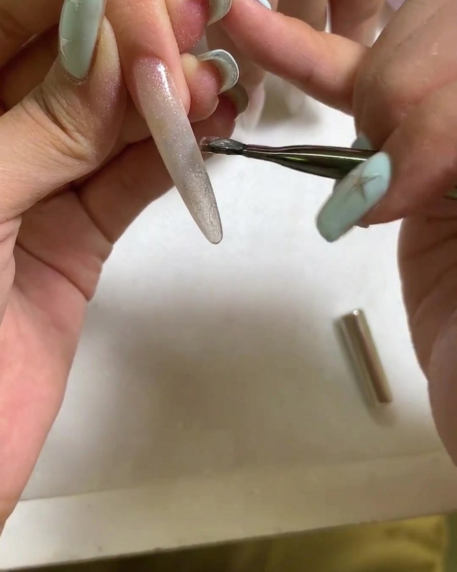 Un outil magnétique tenu près de la surface dun ongle en gel cat eye humide pour former un reflet lumineux brillant et concentré.