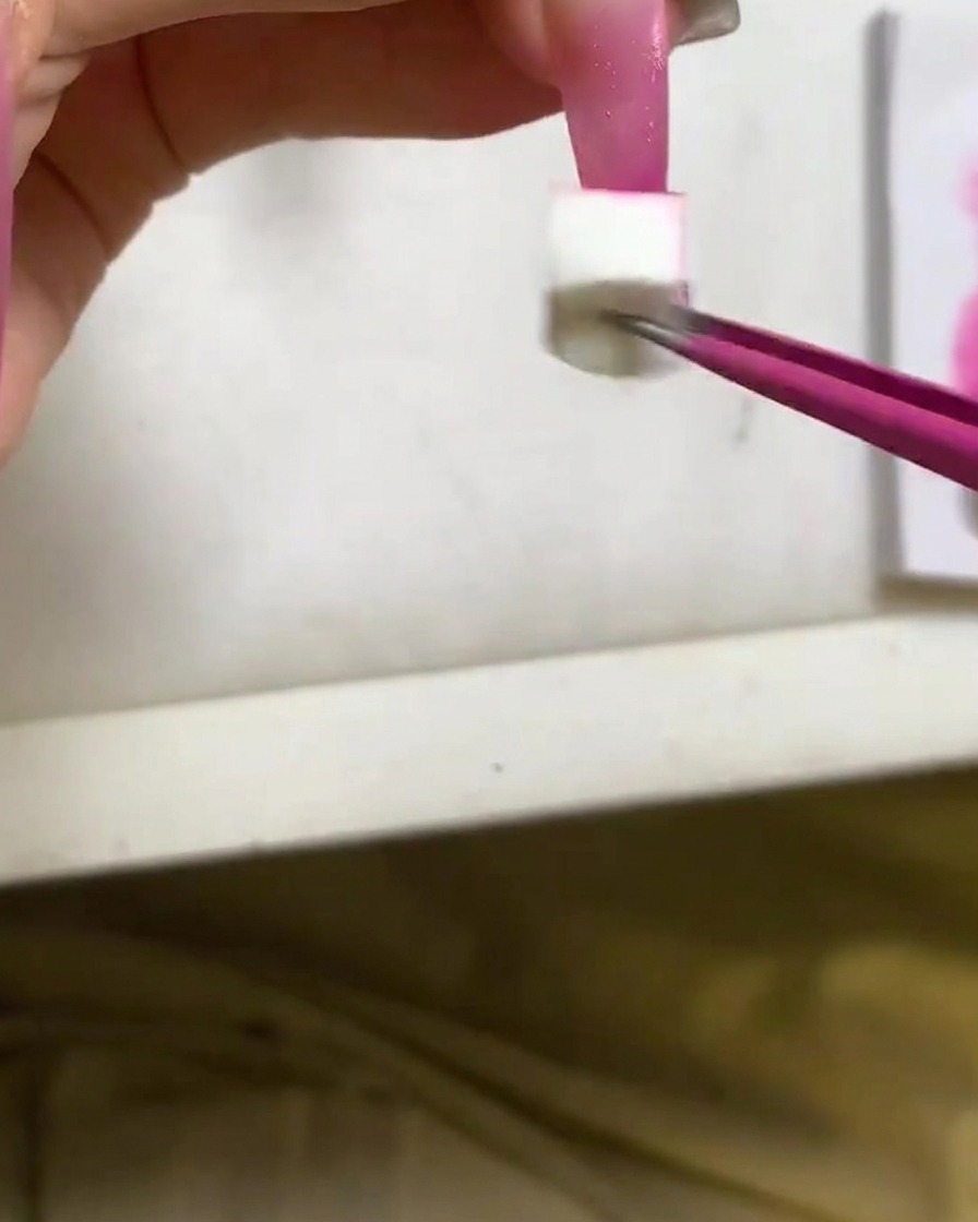 Un applicateur éponge tapotant du vernis gel rouge rose profond sur le bout dun ongle long.