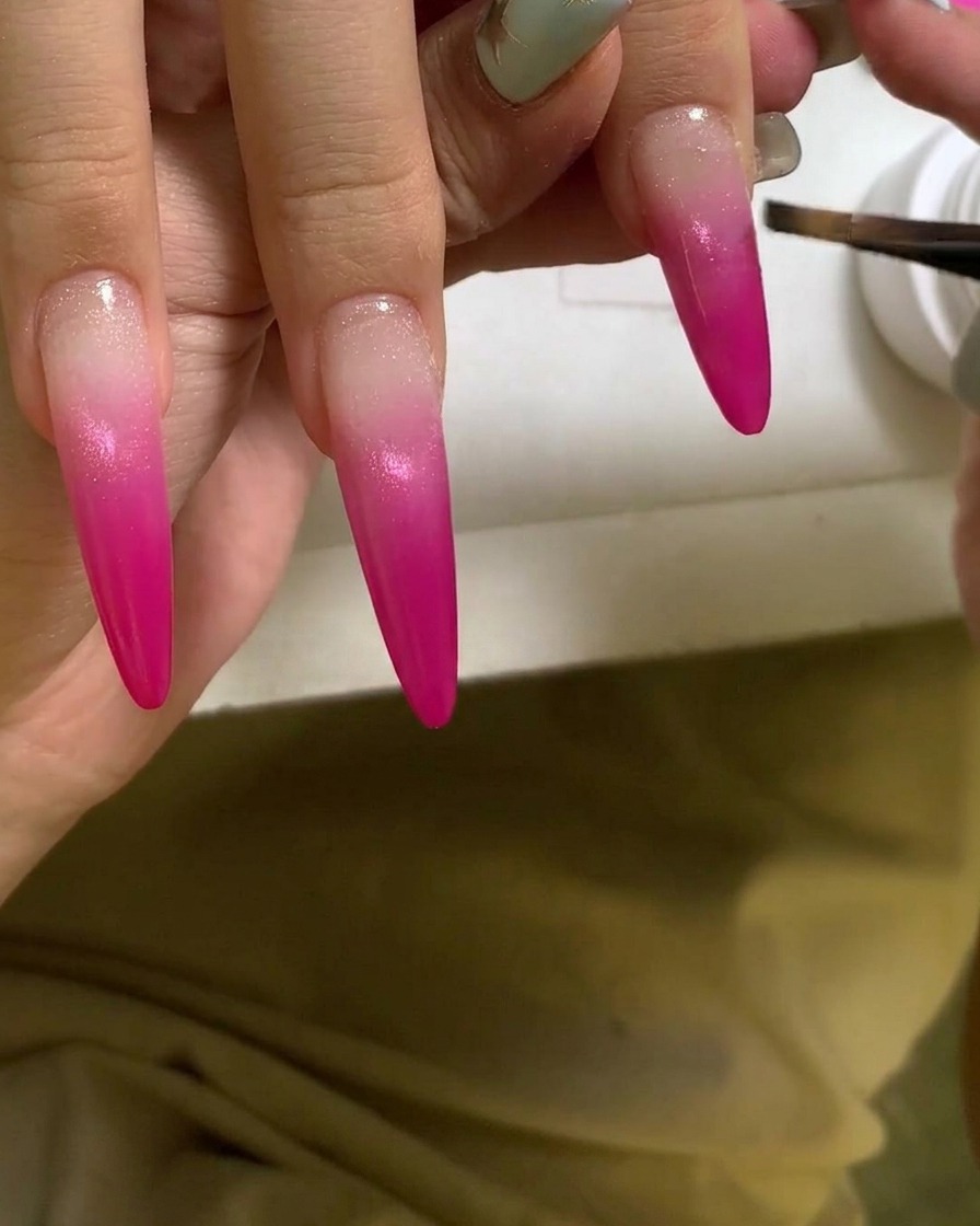 Un pinceau appliquant une couche de gel clair et brillant sur un ongle en dégradé rose vibrant.