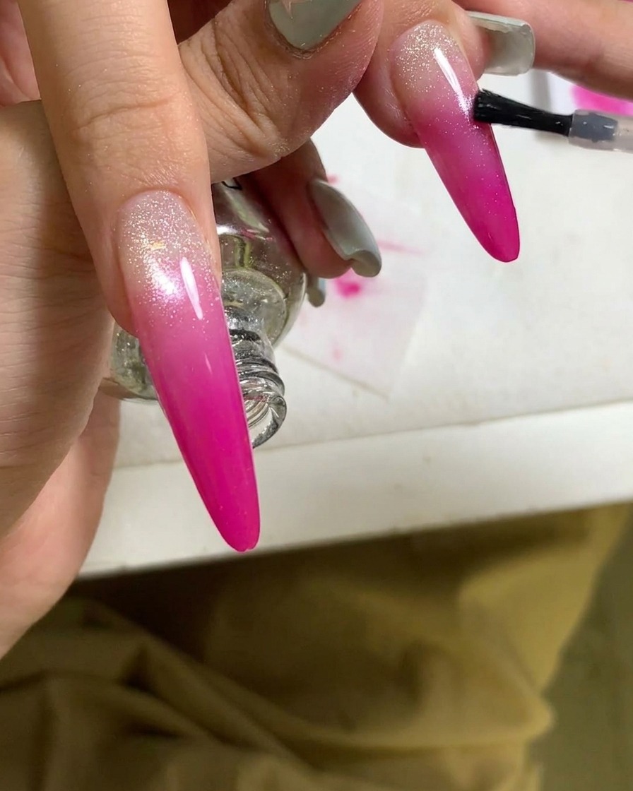 Gros plan dun pinceau appliquant un top coat sur un ongle en dégradé rose fini.