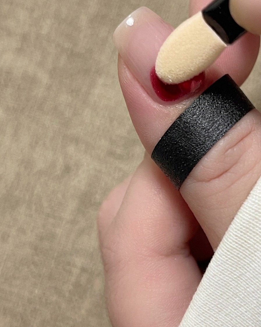 Un applicateur éponge pour fard à paupières tamponnant un pigment dencre rouge à la base dun ongle naturel.