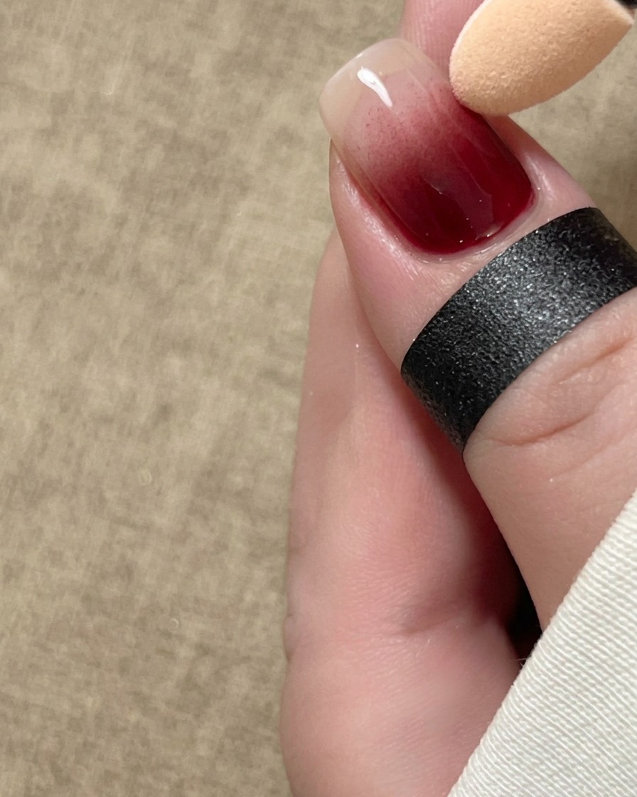 Un applicateur éponge estompant doucement un pigment rouge en dégradé ombré sur la longueur dun ongle.