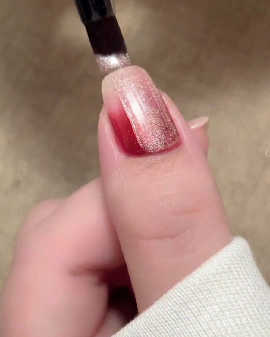 Un coup de pinceau de vernis magnétique cat-eye beige recouvrant la surface de longle.