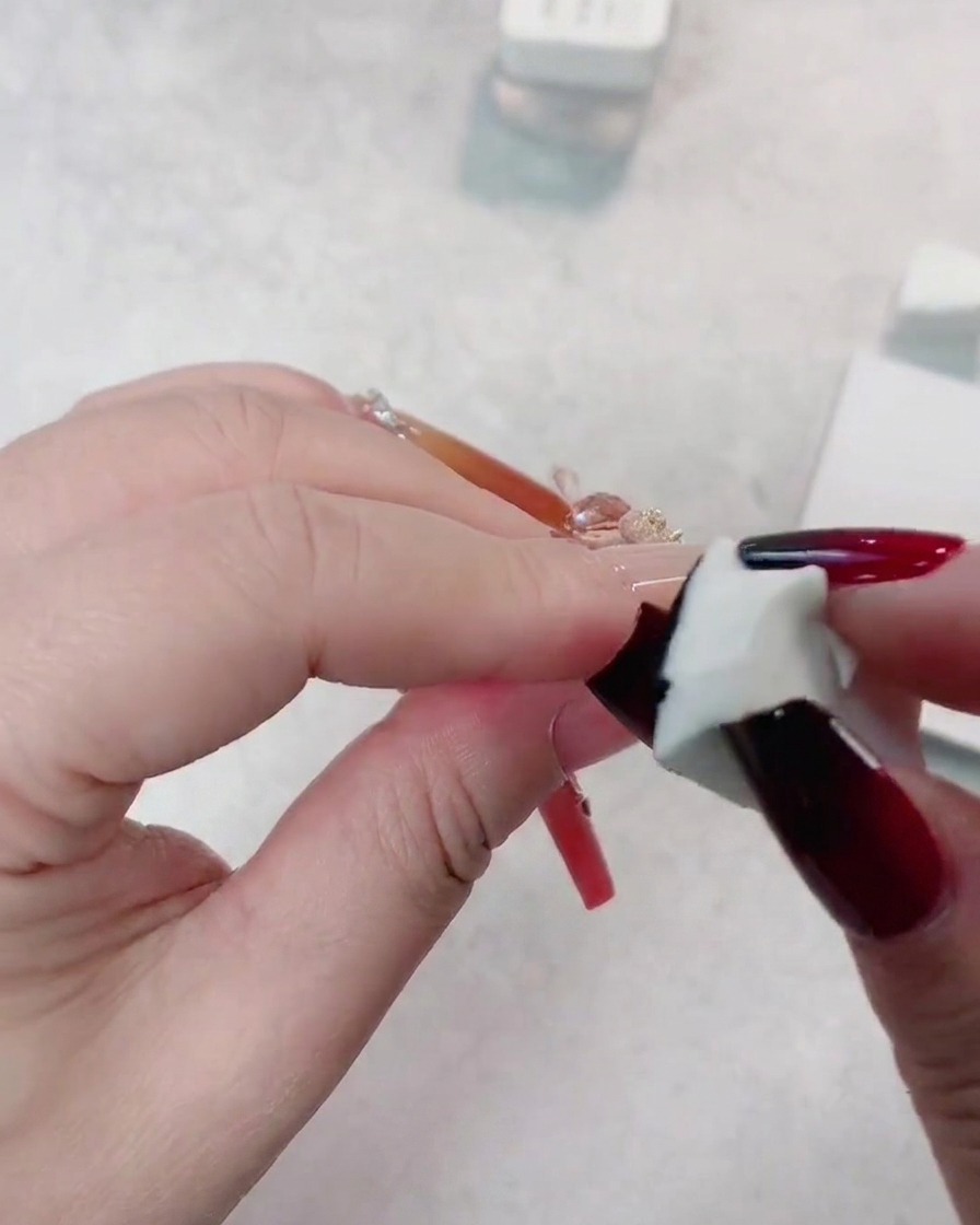 Une éponge appliquant une deuxième couche de gel noir sur le bout dun ongle rouge foncé pour approfondir le dégradé.