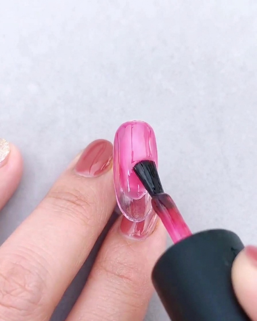 Un pinceau à ongles appliquant une seconde couche de gel rose translucide sur le dégradé existant.