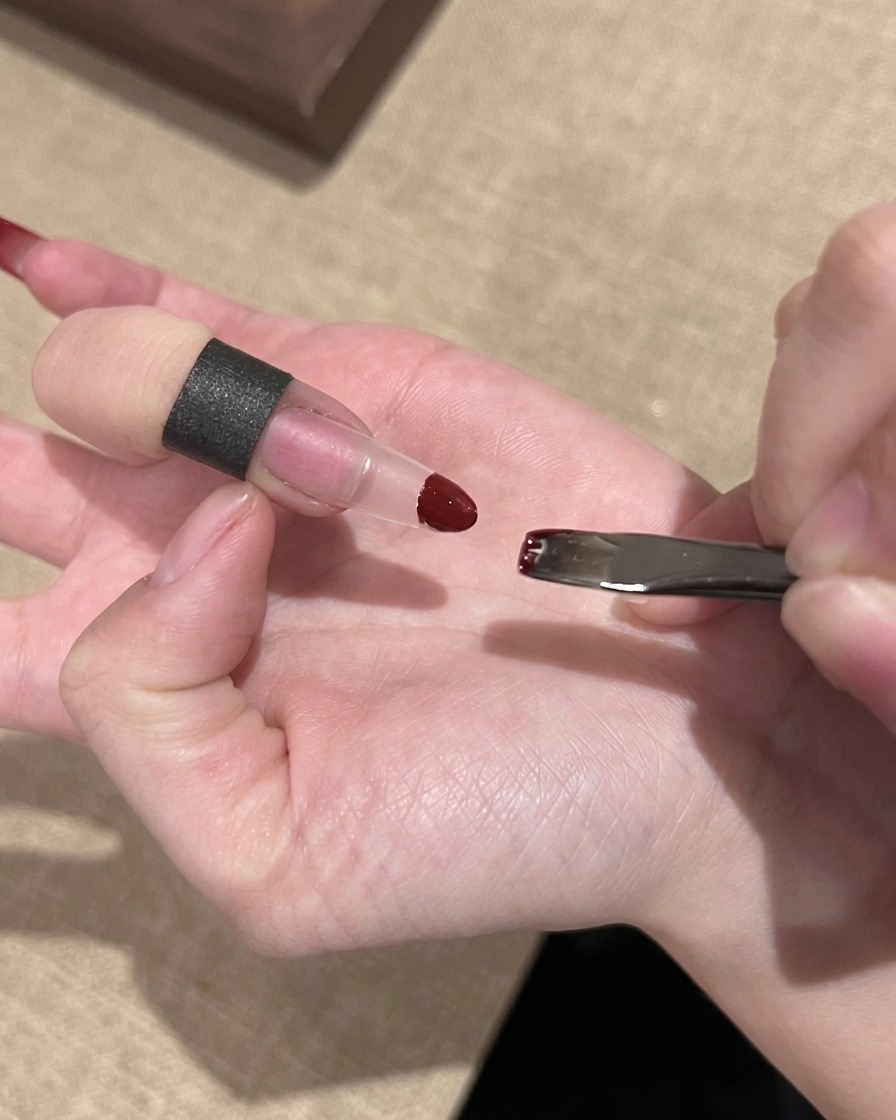 Une main utilisant une petite éponge pour tamponner du vernis gel rouge sur le bout dune extension dongle transparente.