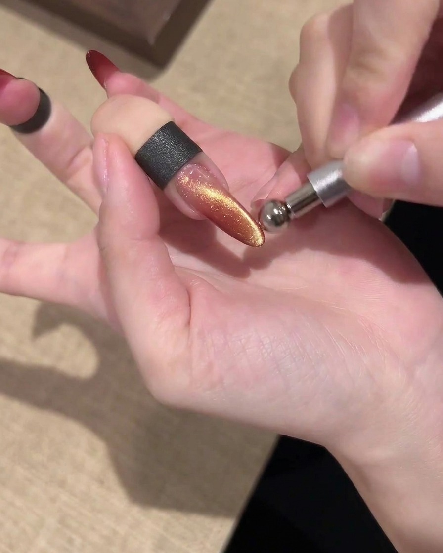 Un aimant barre tenu parallèlement au-dessus dun ongle cat eye doré et rouge chatoyant pour façonner la lumière.