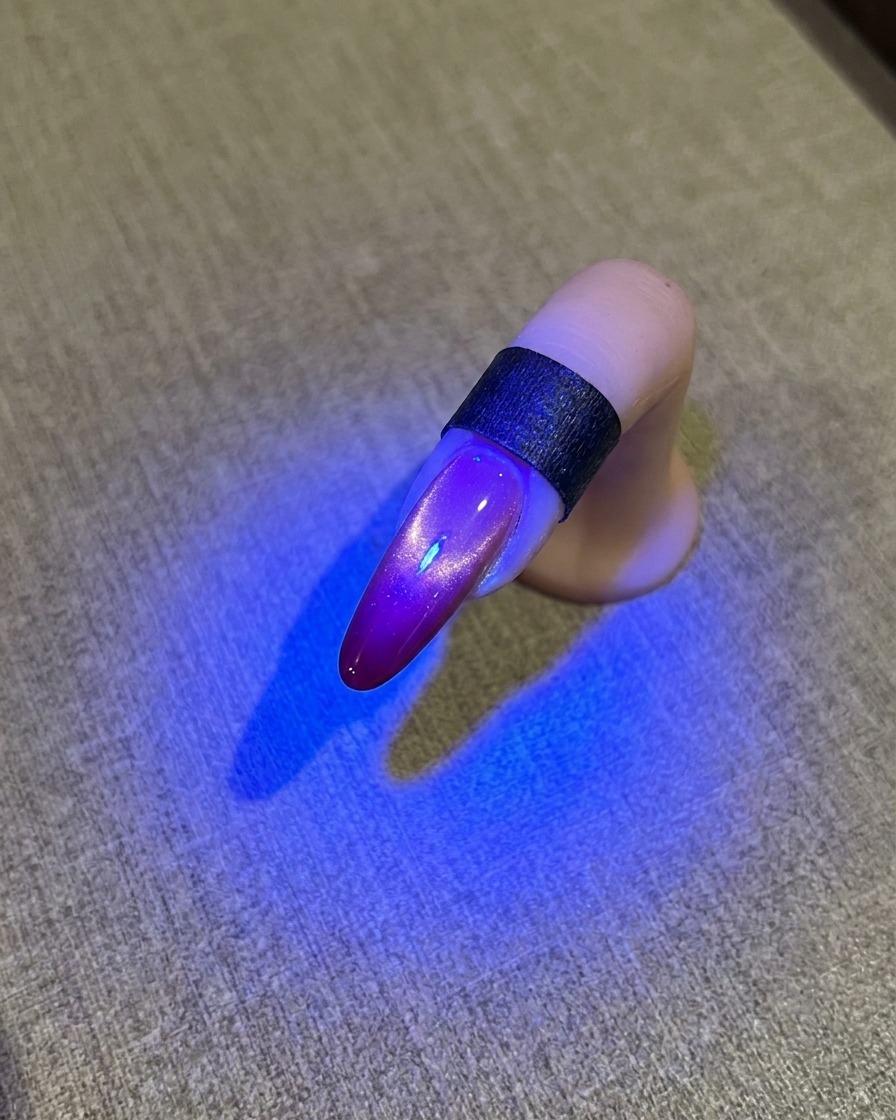 Un ongle sous une lampe UV bleue montrant une finition cat eye brillante.