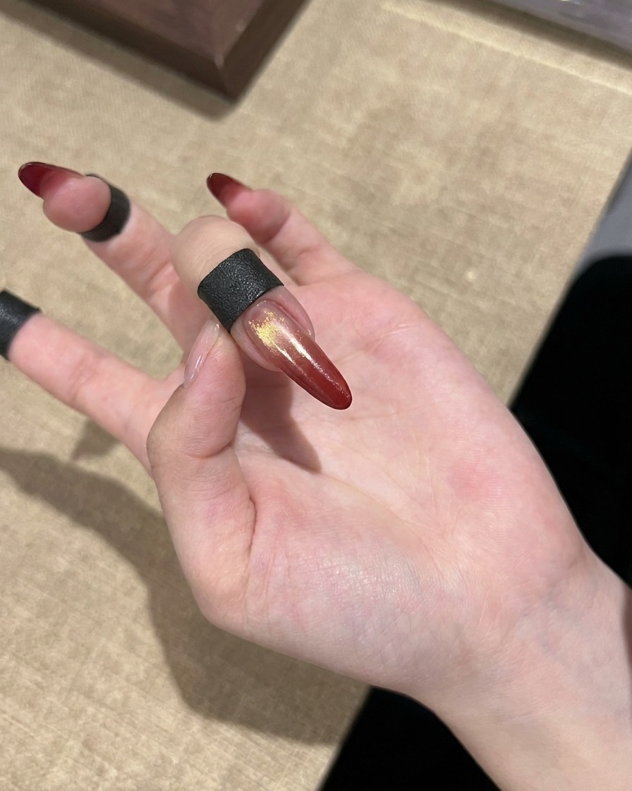 Un ongle cat eye en dégradé rouge fini avec des accents dorés présenté sur une main.