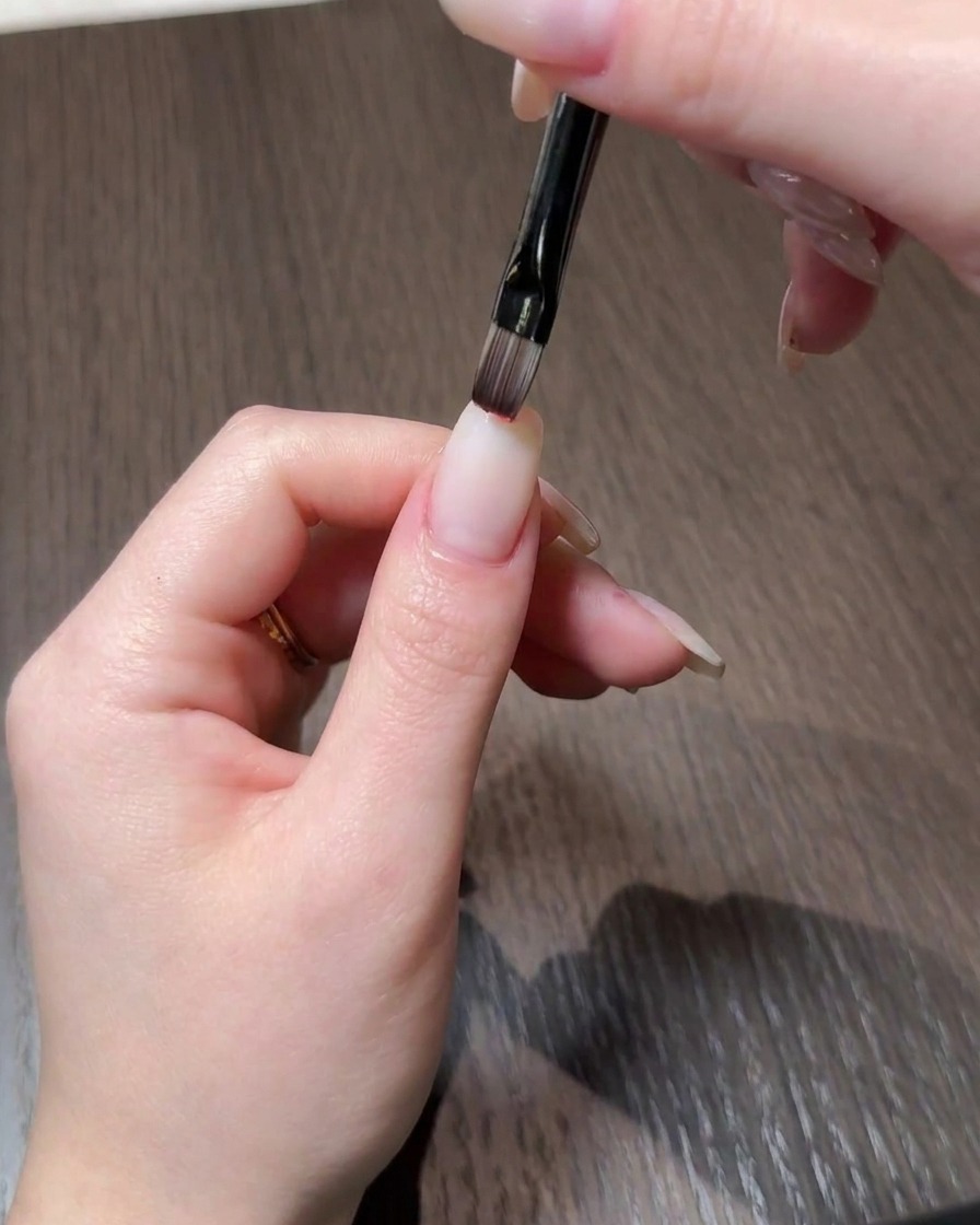 Gros plan dune main appliquant du vernis gel rouge sur le bout dun ongle dapparence naturelle à laide dun pinceau fin.