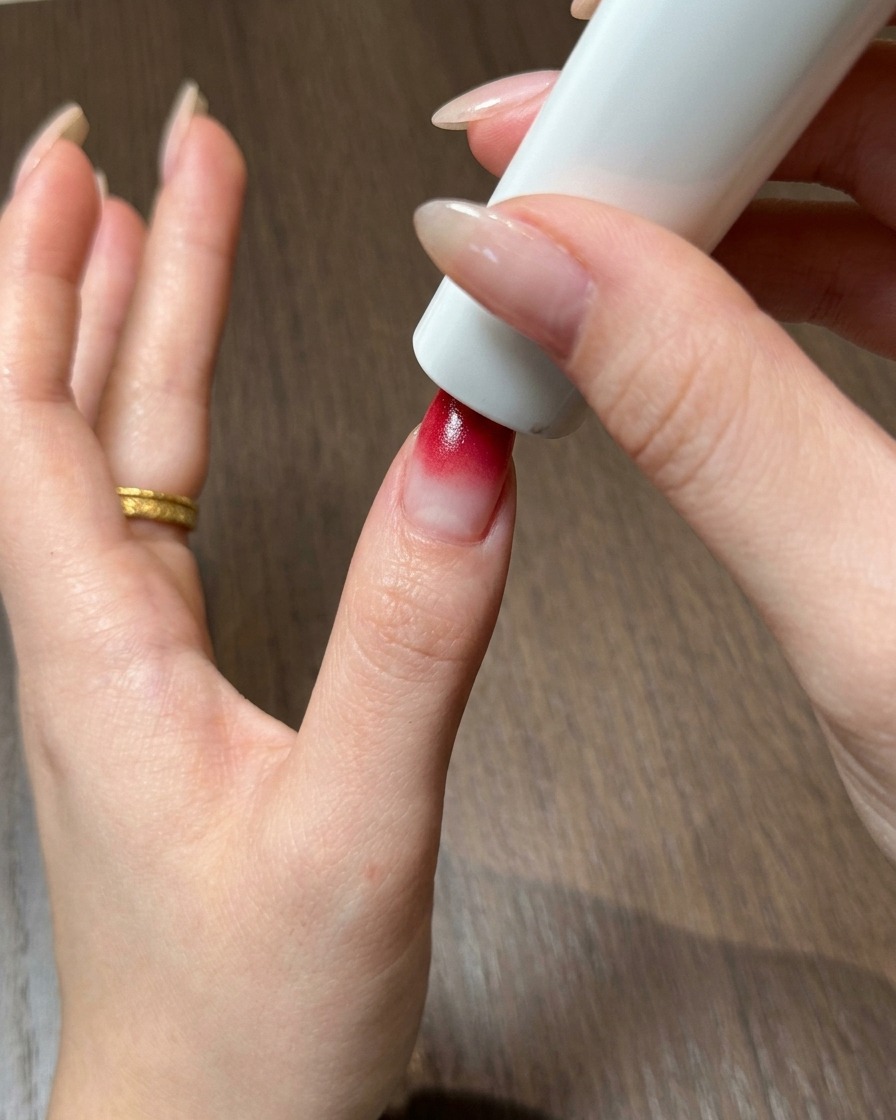 Un pouce positionné directement sous une lampe UV et LED portable pour catalyser le gel ombré rouge.