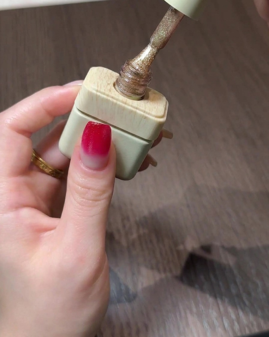 Un flacon de gel cat eye doré avec son pinceau posé au-dessus dun ongle en dégradé.