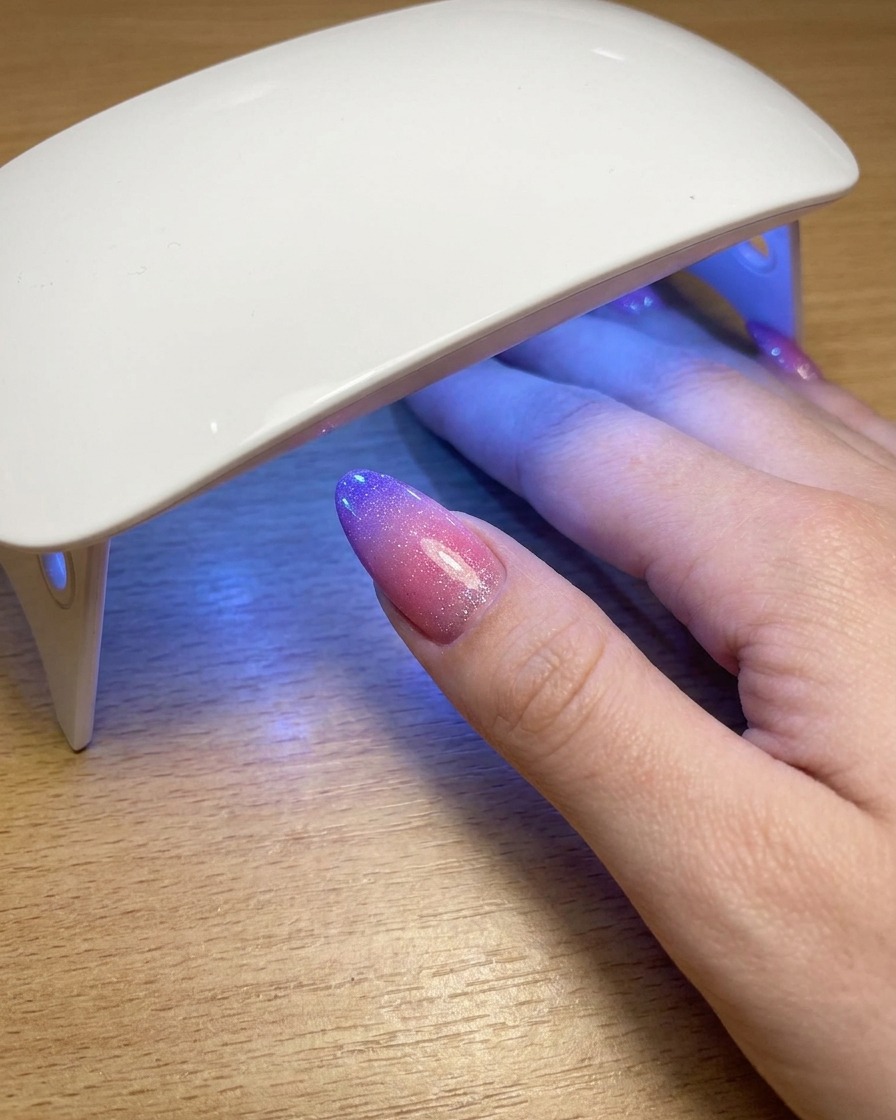 Un pouce reposant sous une lampe UV portable pendant la catalysation de la couche finale de vernis gel cat eye.