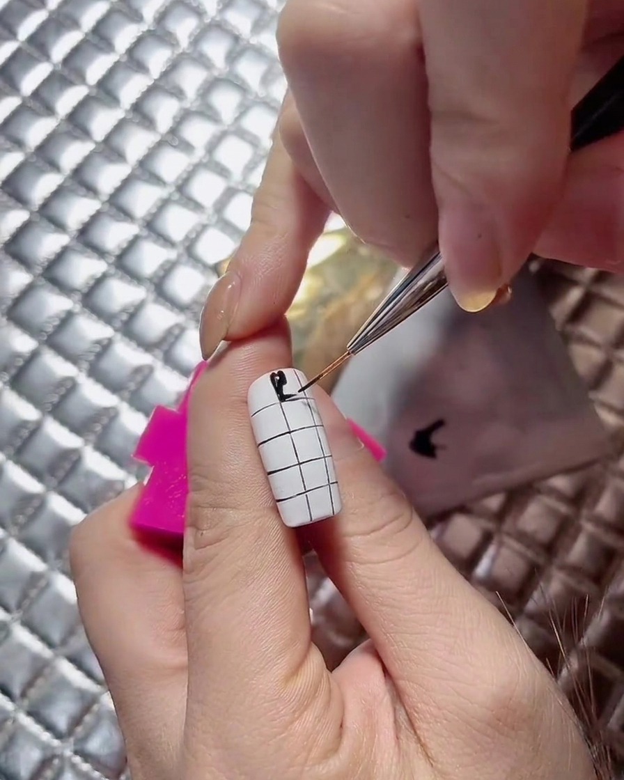 Une prothésiste ongulaire poursuivant les carrés noirs alternés le long dun design dongle en damier.