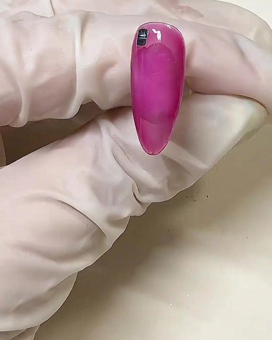 Gros plan dun ongle rose avec un seul carré métallique argenté placé près de la ligne cuticulaire sur de la colle solide non catalysée.