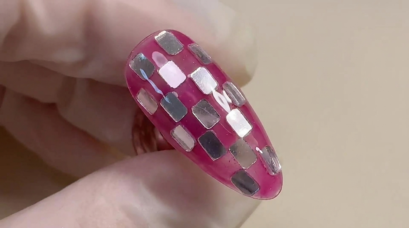 Gros plan sur le nail art fini en damier miroir rose et argent, mettant en valeur une base translucide brillante et des carrés de feuille métallique incrustés.