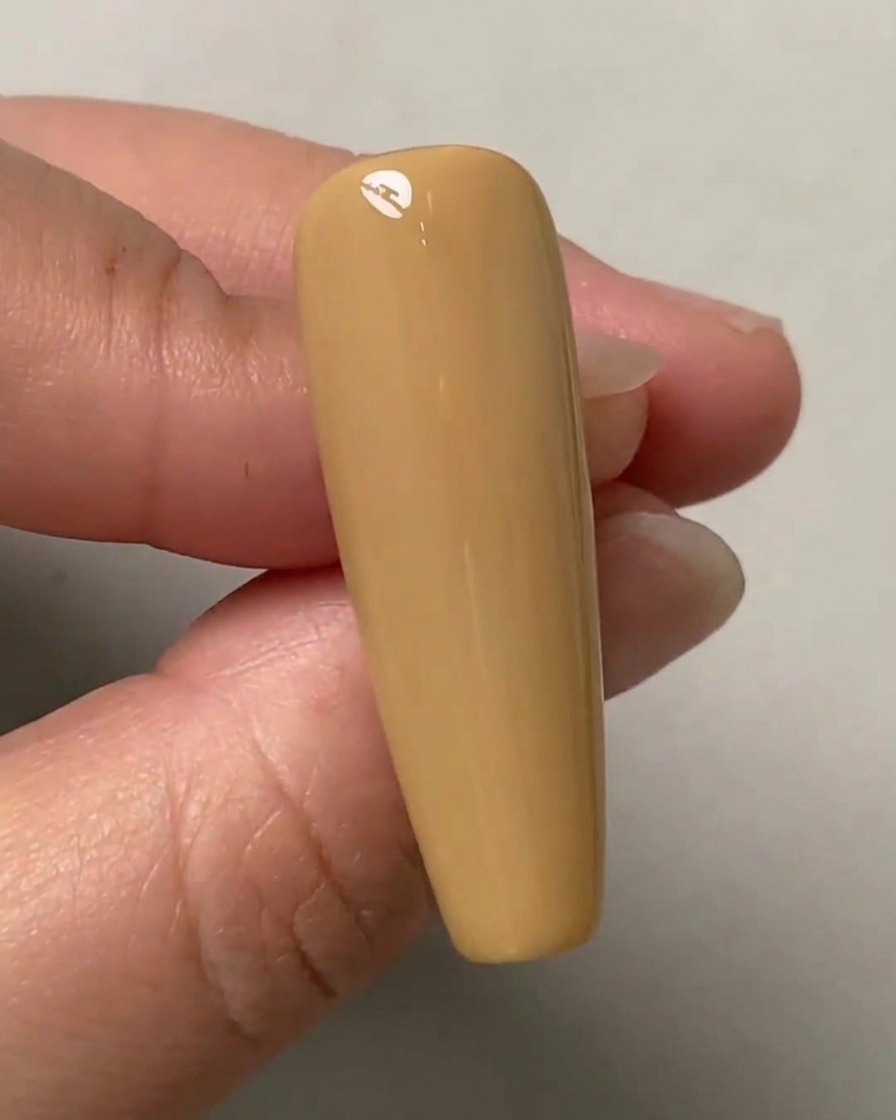 Une main tenant un ongle dentraînement de couleur nude avec trois petits points marqués verticalement au centre.