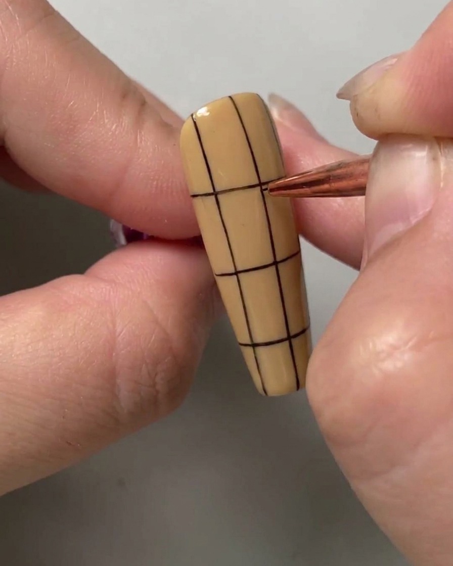 Un pinceau de nail art dessinant une ligne noire horizontale sur la moitié supérieure dun ongle rayé verticalement.
