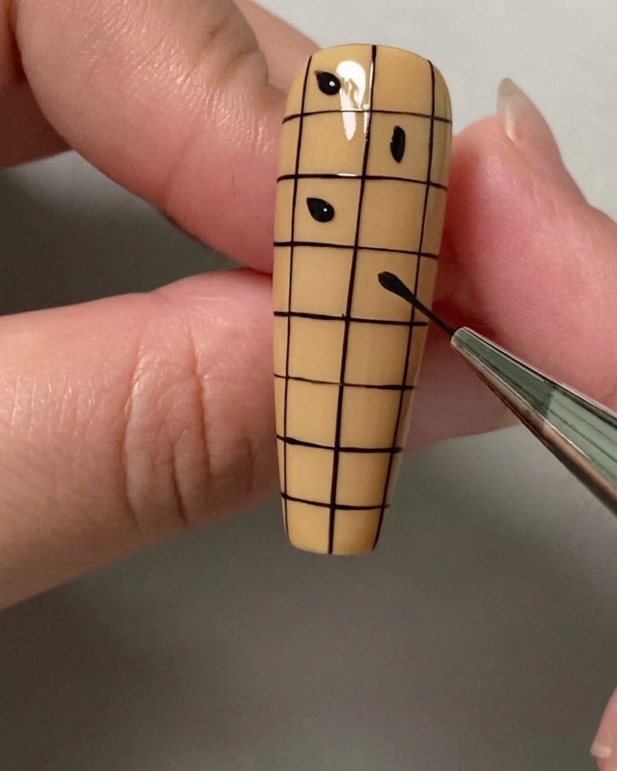 Un dotting tool ou pinceau plaçant de petits points noirs dans des carrés alternés dun quadrillage sur un ongle.