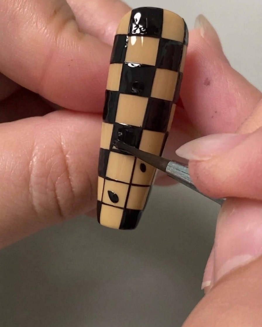 Gros plan dun pinceau de détail remplissant un petit carré de vernis noir pour créer un motif damier sur un ongle.