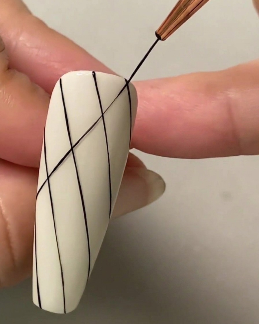 Un pinceau fin dessinant une ligne noire diagonale croisant les lignes parallèles existantes pour former un motif quadrillé de losanges.