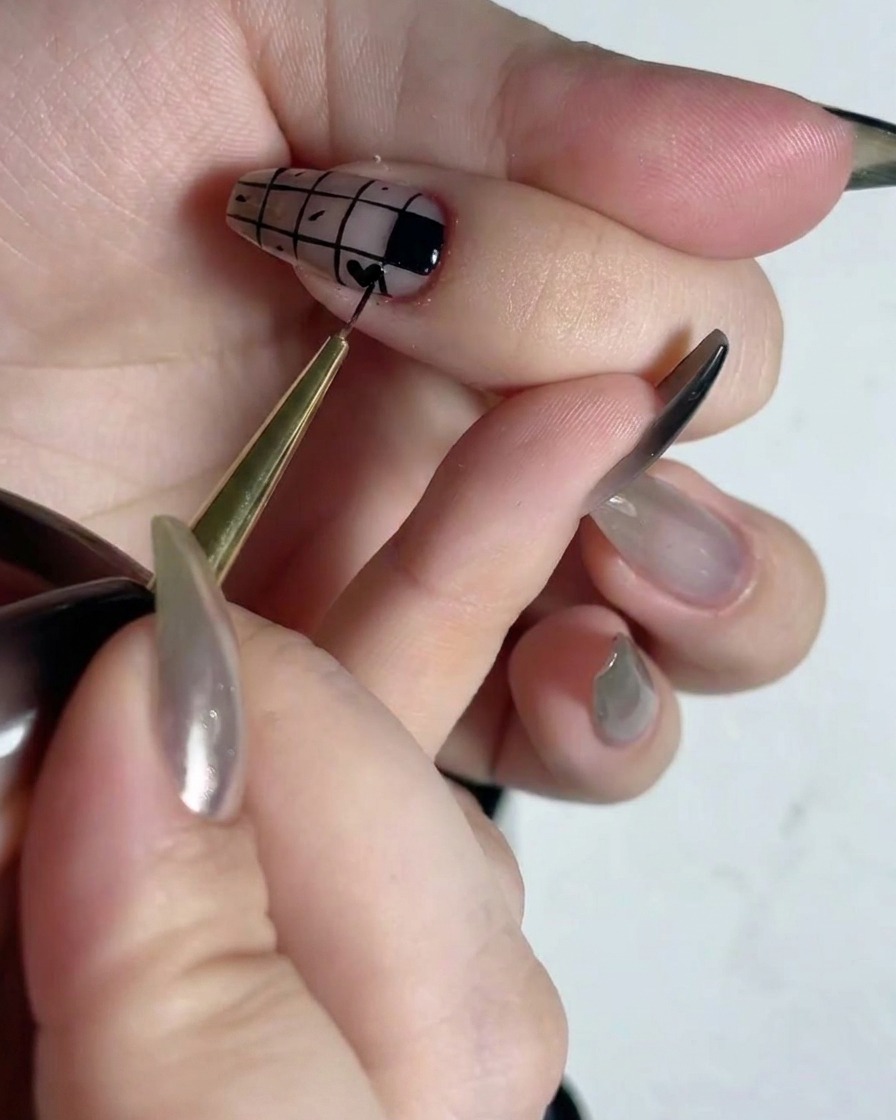 Un pinceau de détail fin remplissant de vernis noir des carrés alternés dun motif de grille sur un ongle.