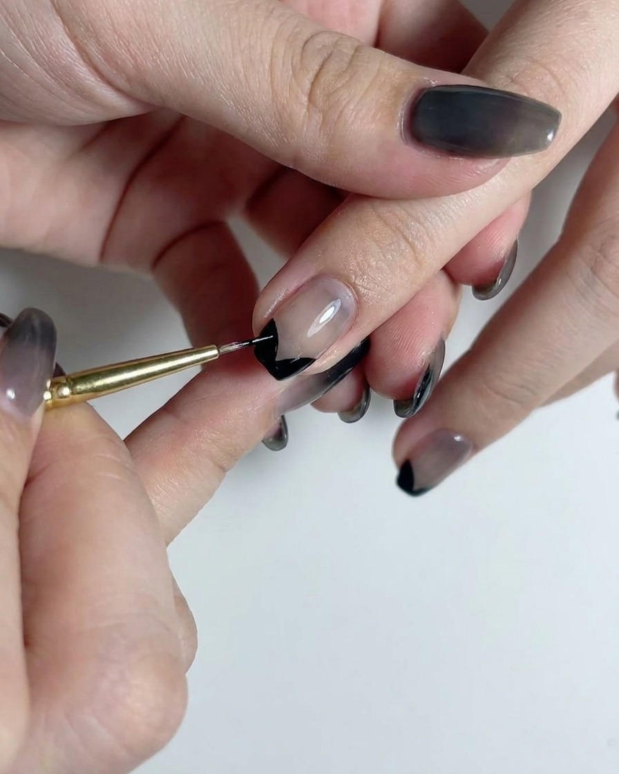 Un pinceau liner fin traçant une ligne noire verticale droite au centre dun ongle à dégradé translucide fumé.