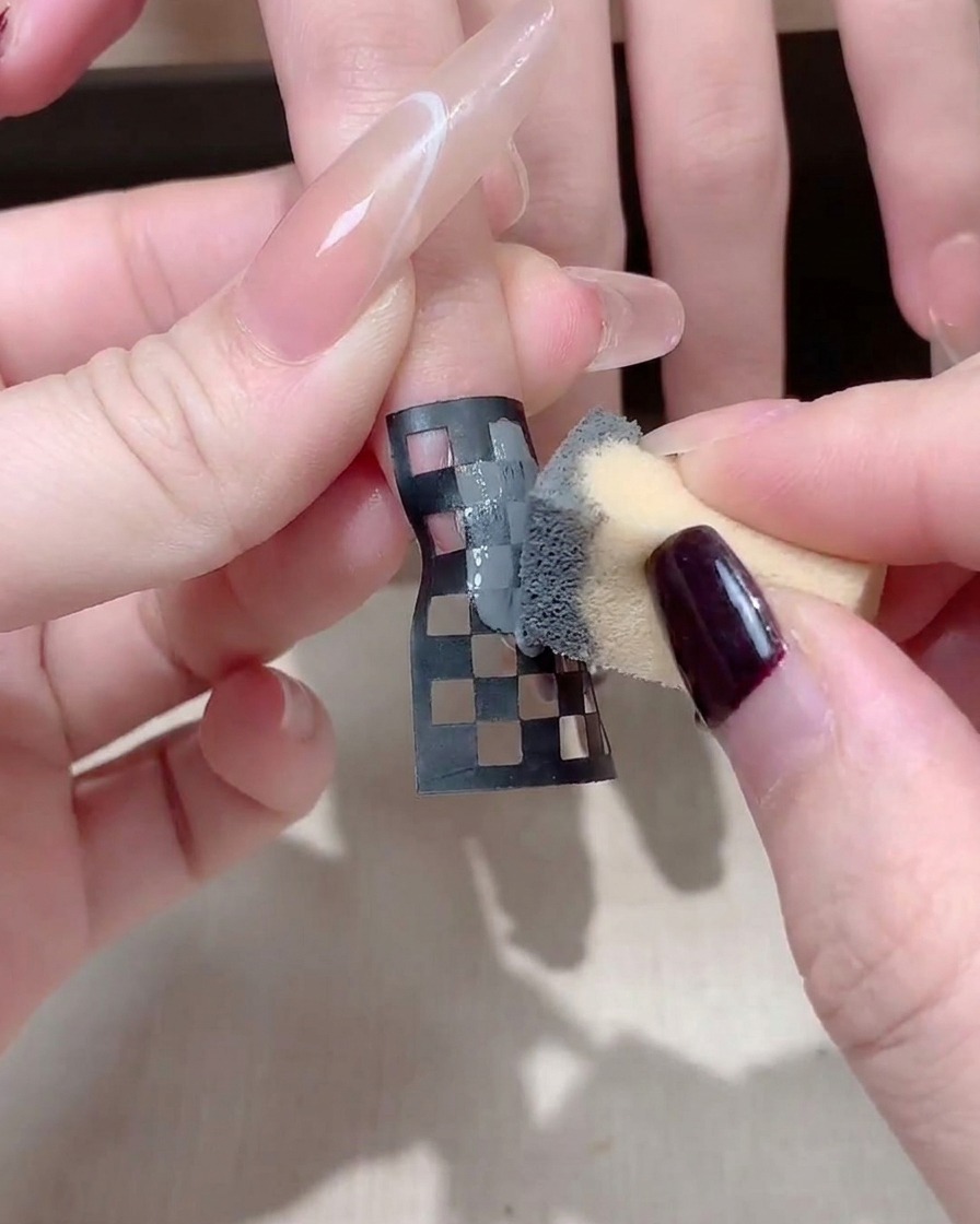 Gros plan dune prothésiste ajustant un sticker damier noir et blanc sur un ongle long et carré.