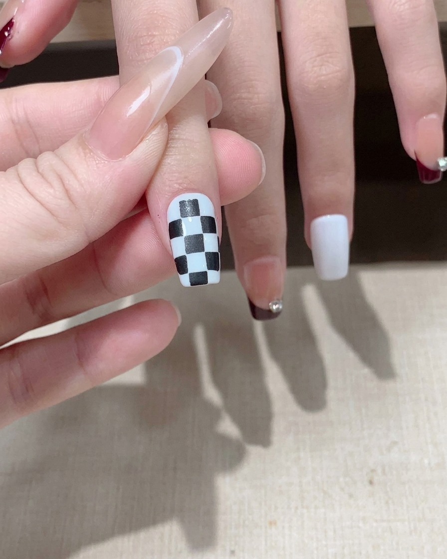 Un pinceau appliquant un top coat brillant sur un motif damier noir et blanc terminé.