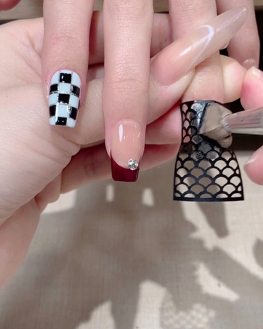 Une pince à épiler retirant délicatement un sticker résille noir dun ongle, révélant un motif en dessous.