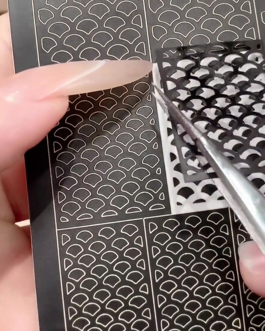 Une pince à épiler décollant une planche de stickers nail art noirs usagée pour montrer sa réutilisation.