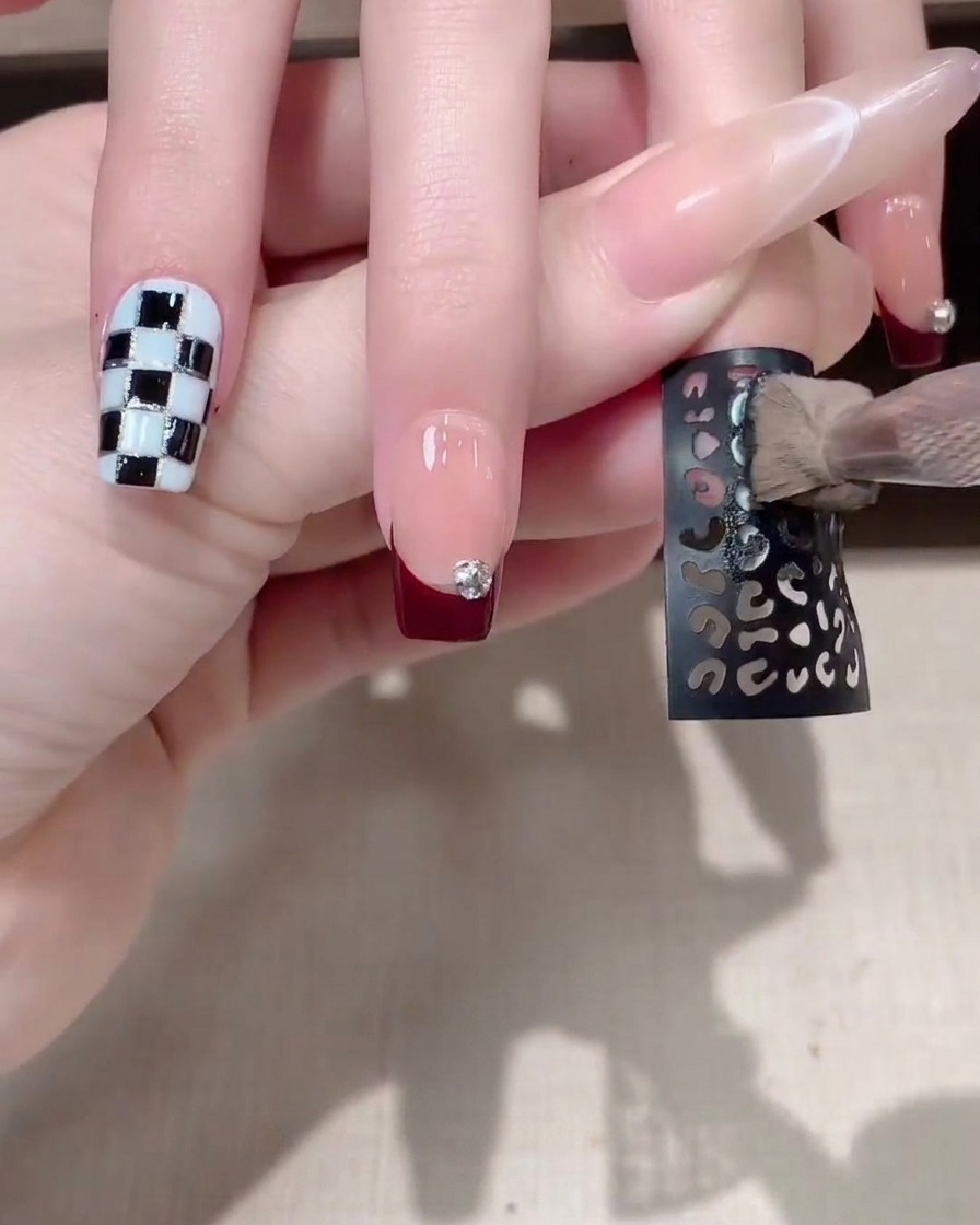Un sticker à motif sombre ajouré en cours dapplication sur un ongle manucuré.