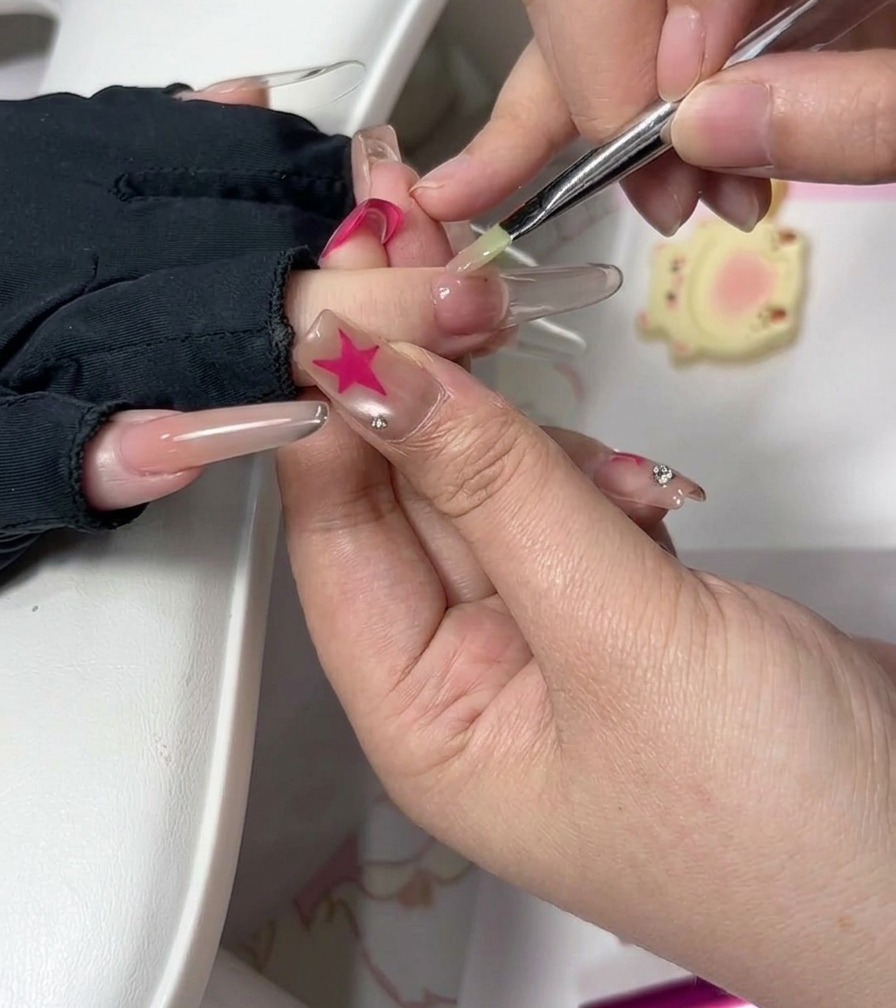 Une prothésiste ongulaire utilisant un pinceau fin pour lisser soigneusement le gel près des cuticules sur un ongle rallongé.