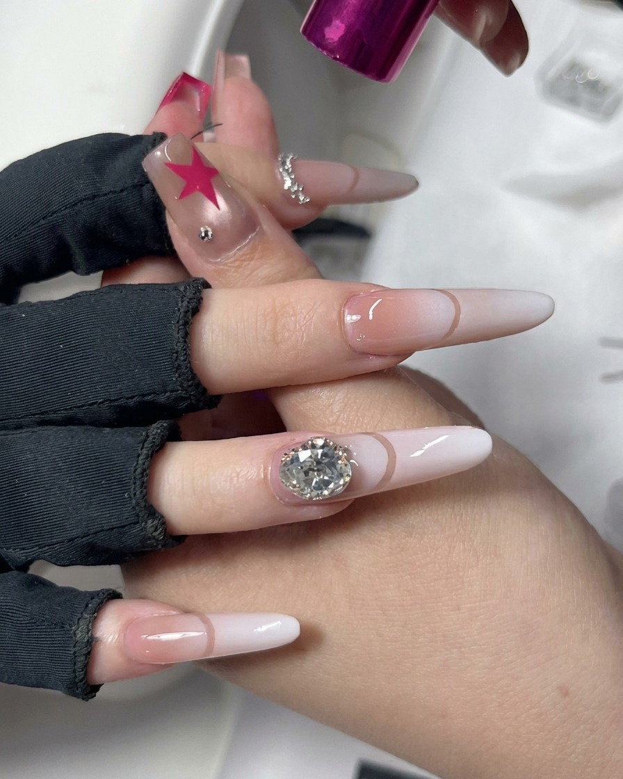 Une main positionnée sous une lampe de catalysation UV/LED rose compacte avec du nail art décoratif.