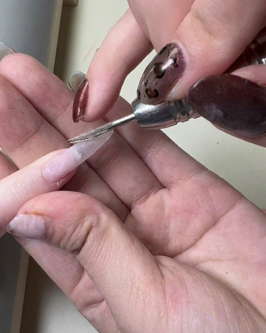 Un pinceau appliquant une fine couche de gel gris translucide sur une extension dongle longue préparée.