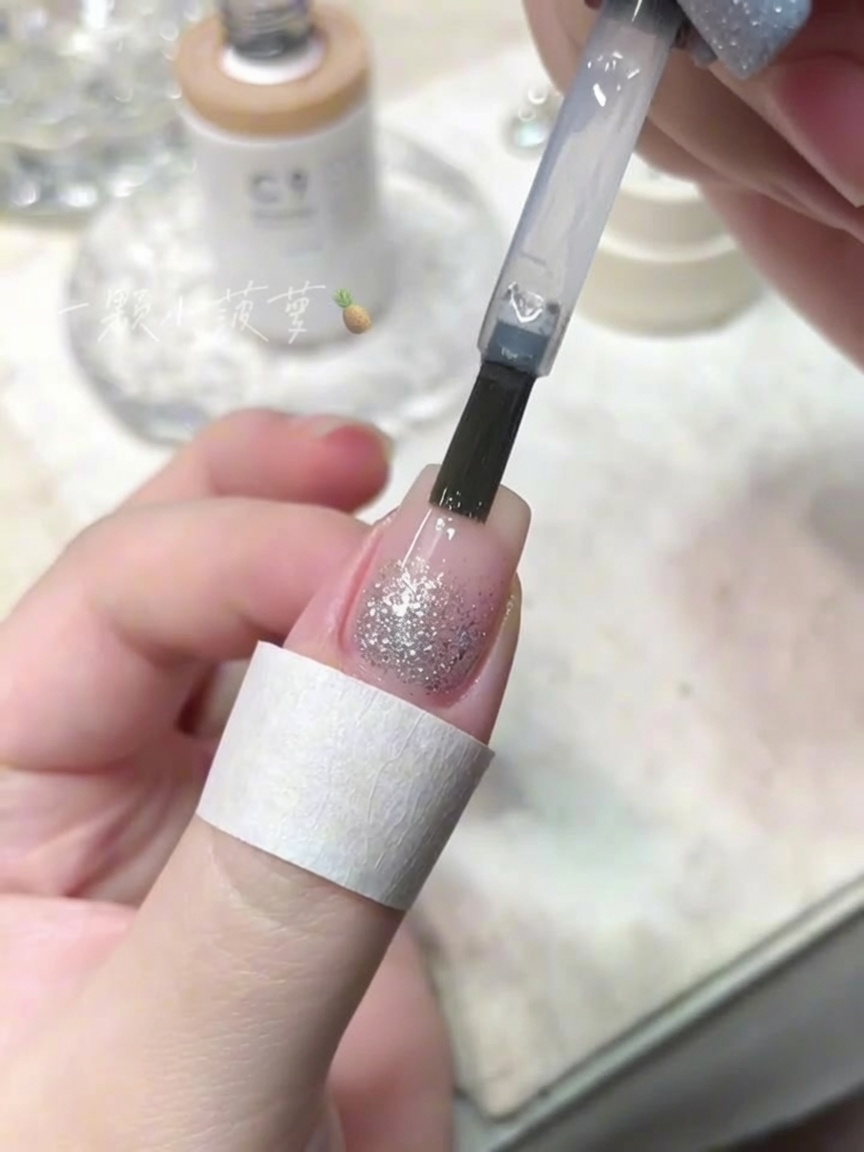 Un pinceau de flacon appliquant un top coat transparent sur un ongle avec des paillettes diamant.