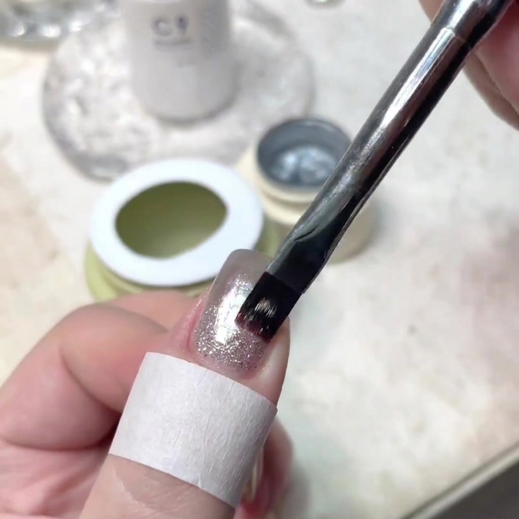Un pinceau à ongles appliquant précisément un fin trait de gel scintillant au centre dun ongle manucuré.