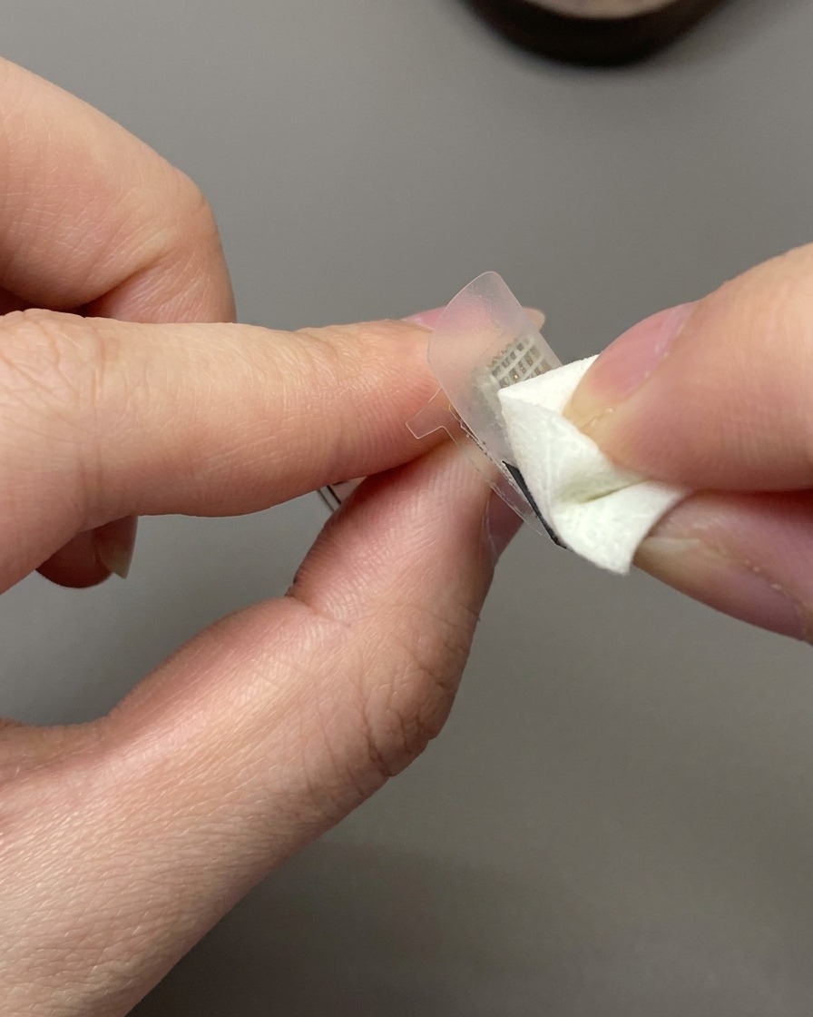 Une éponge de maquillage tamponnant du vernis gel blanc cassé sur un sticker guide French posé sur un ongle.