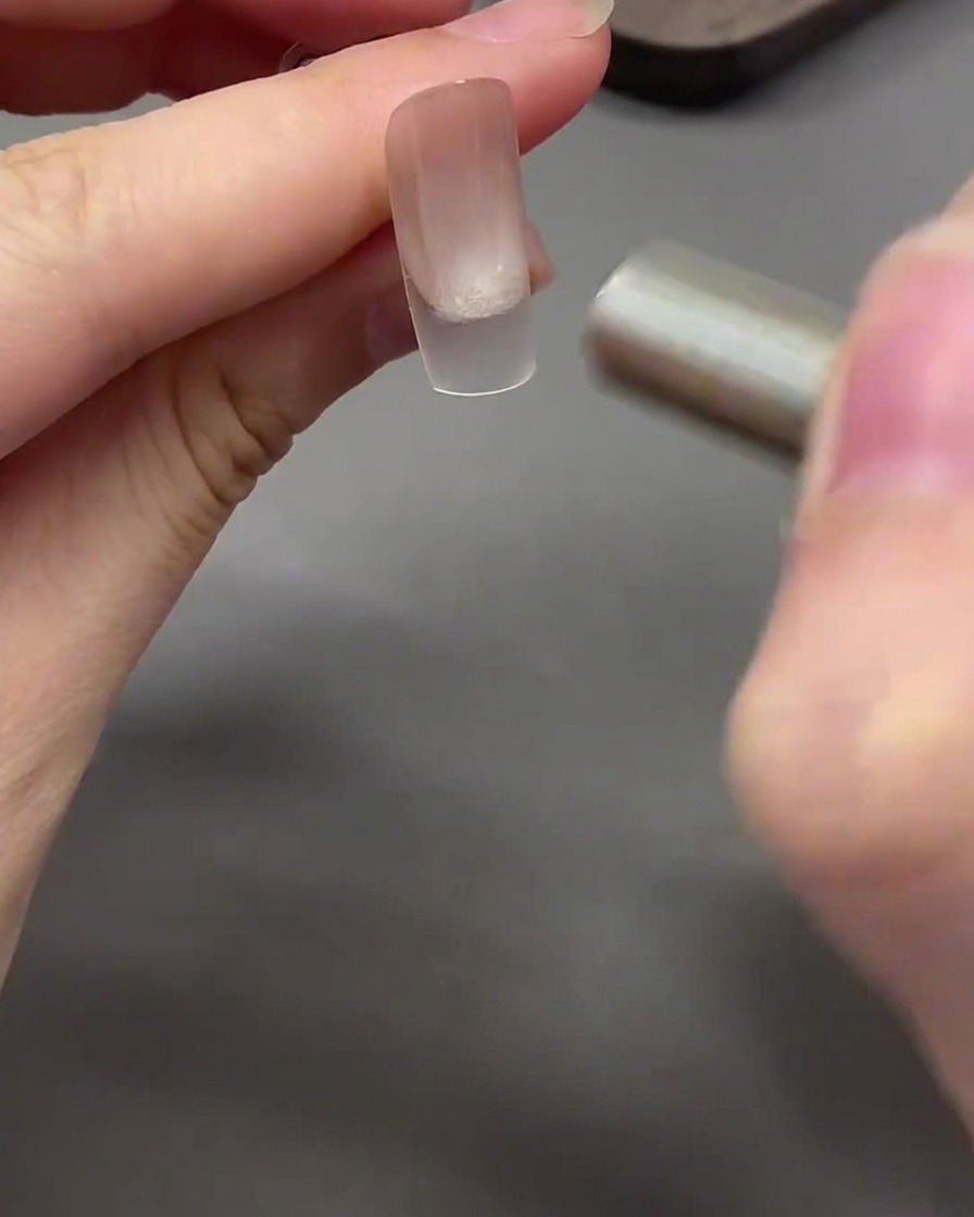 Un aimant effectuant un mouvement incurvé autour de la pointe de longle pour modeler le gel cat eye en un effet perle de verre.