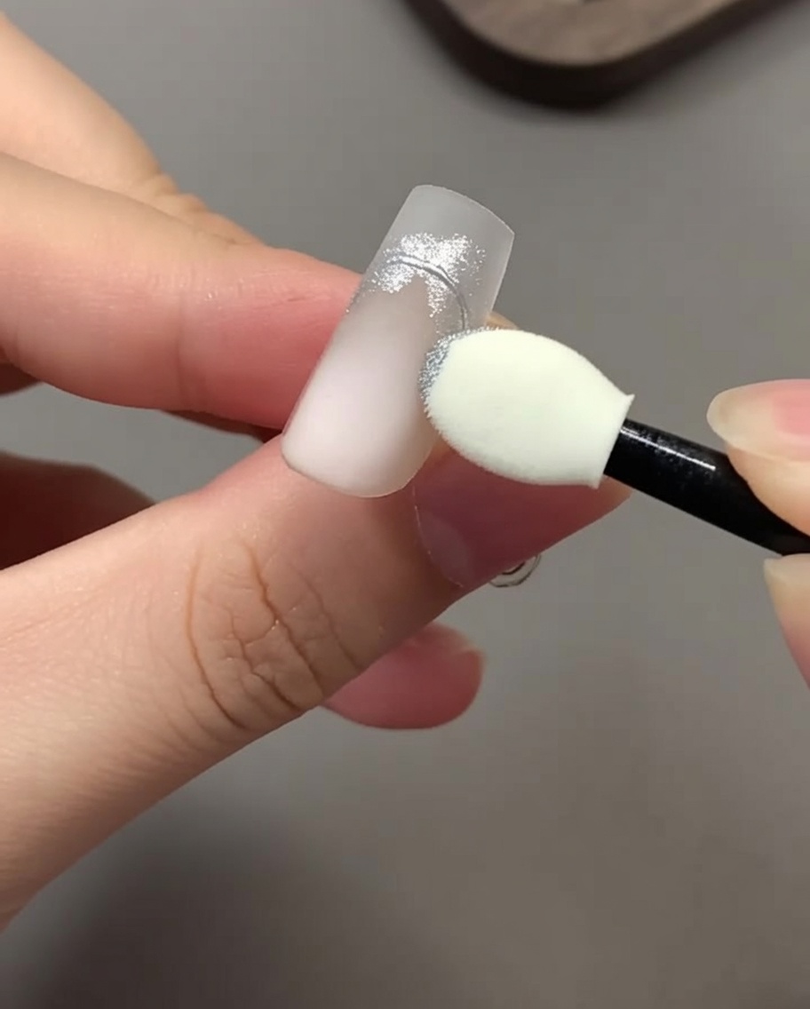 Un applicateur éponge pour fard à paupières frottant de la poudre chrome argentée sur un design dongle.