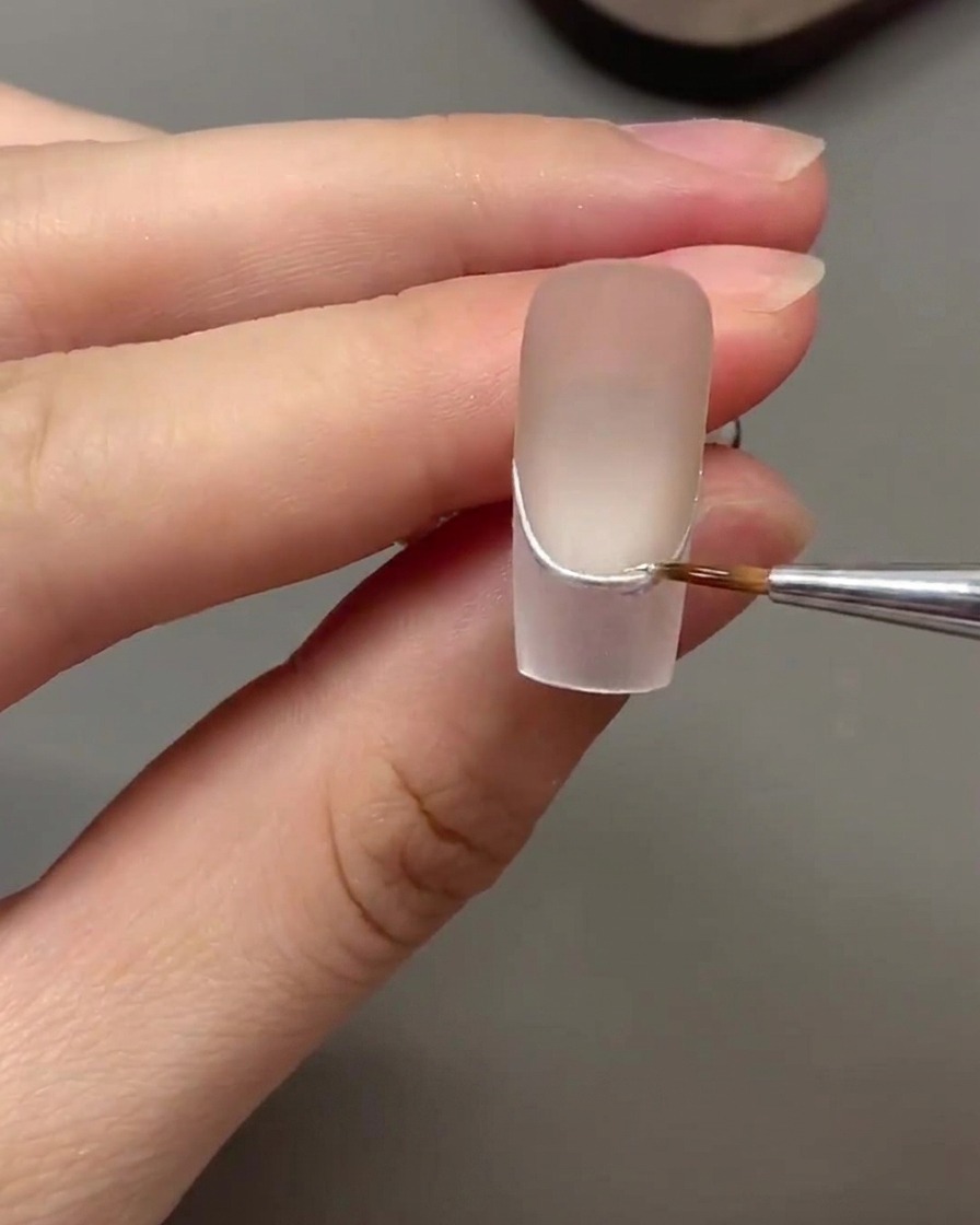 Un pinceau fin appliquant une couche protectrice de gel de renforcement transparent sur une ligne en chrome argenté.