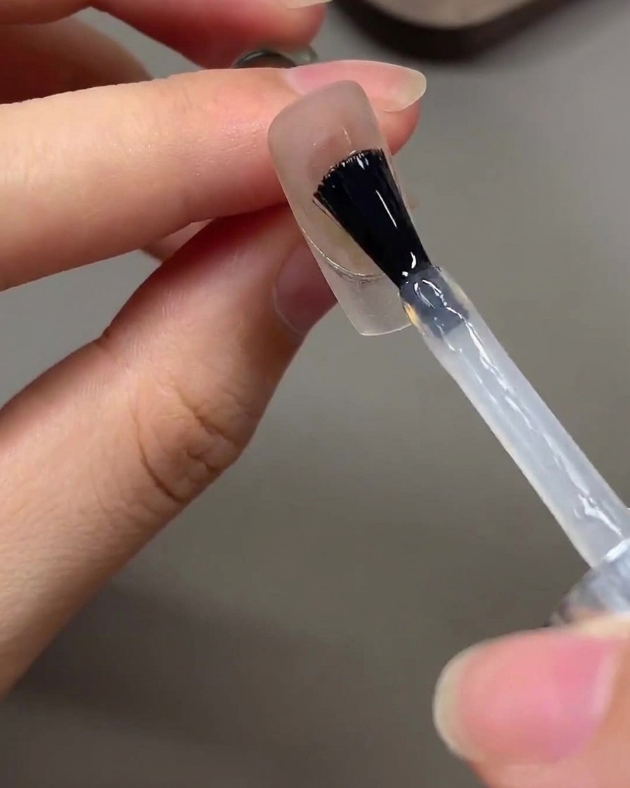 Un pinceau appliquant un top coat brillant transparent sur un design dongle terminé.