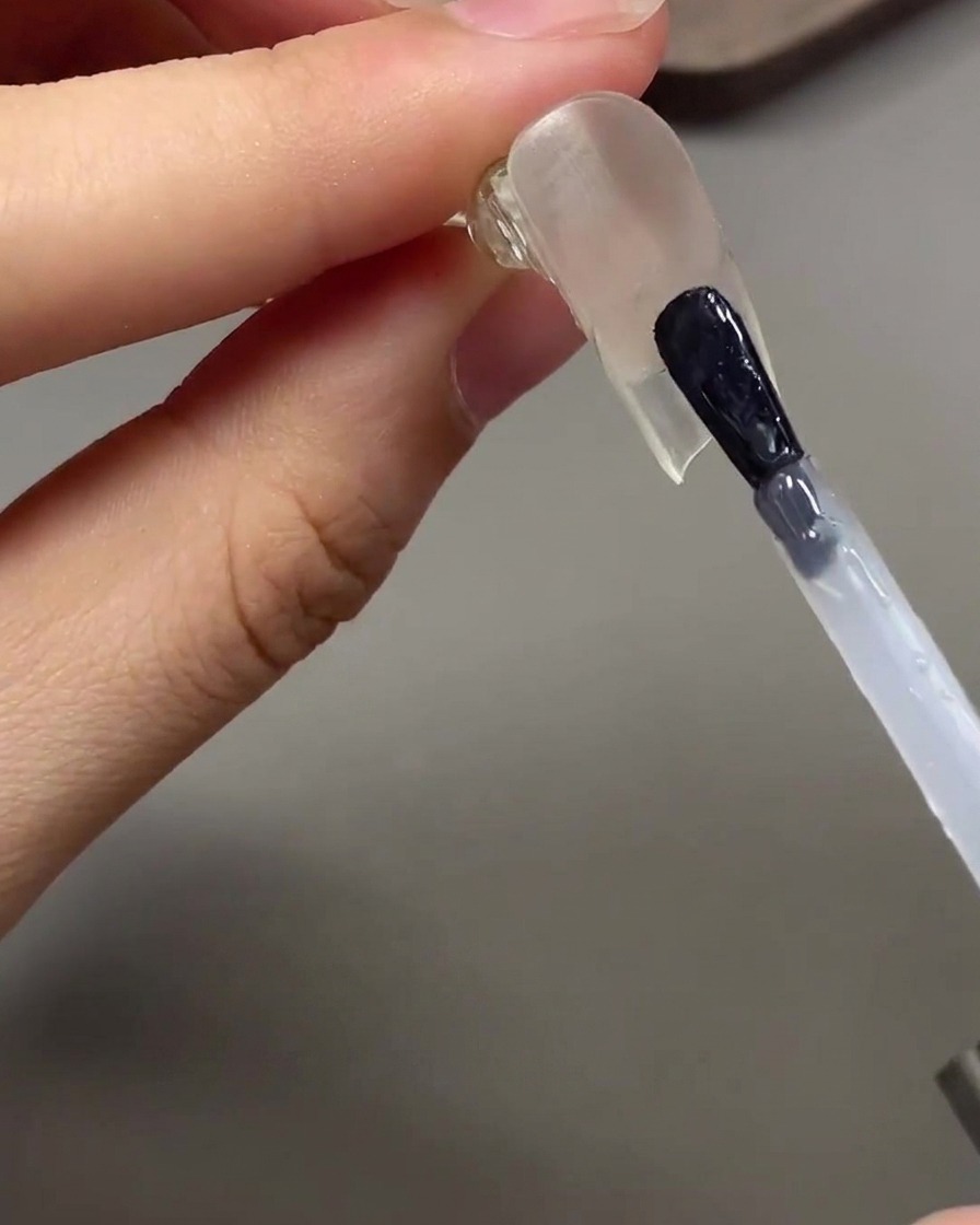Un pinceau appliquant un top coat brillant transparent sous la pointe dongle prolongée.