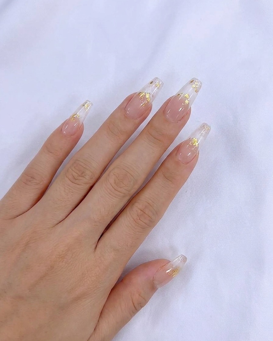 Un pinceau appliquant une couche uniforme de vernis gel nude transparent sur longle naturel.
