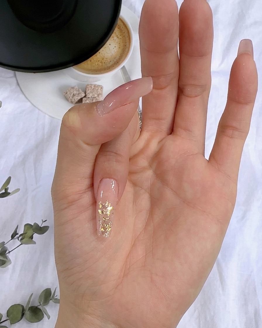 Gros plan de flocons de feuille dor pressés sur la couche de paillettes humides dun ongle.