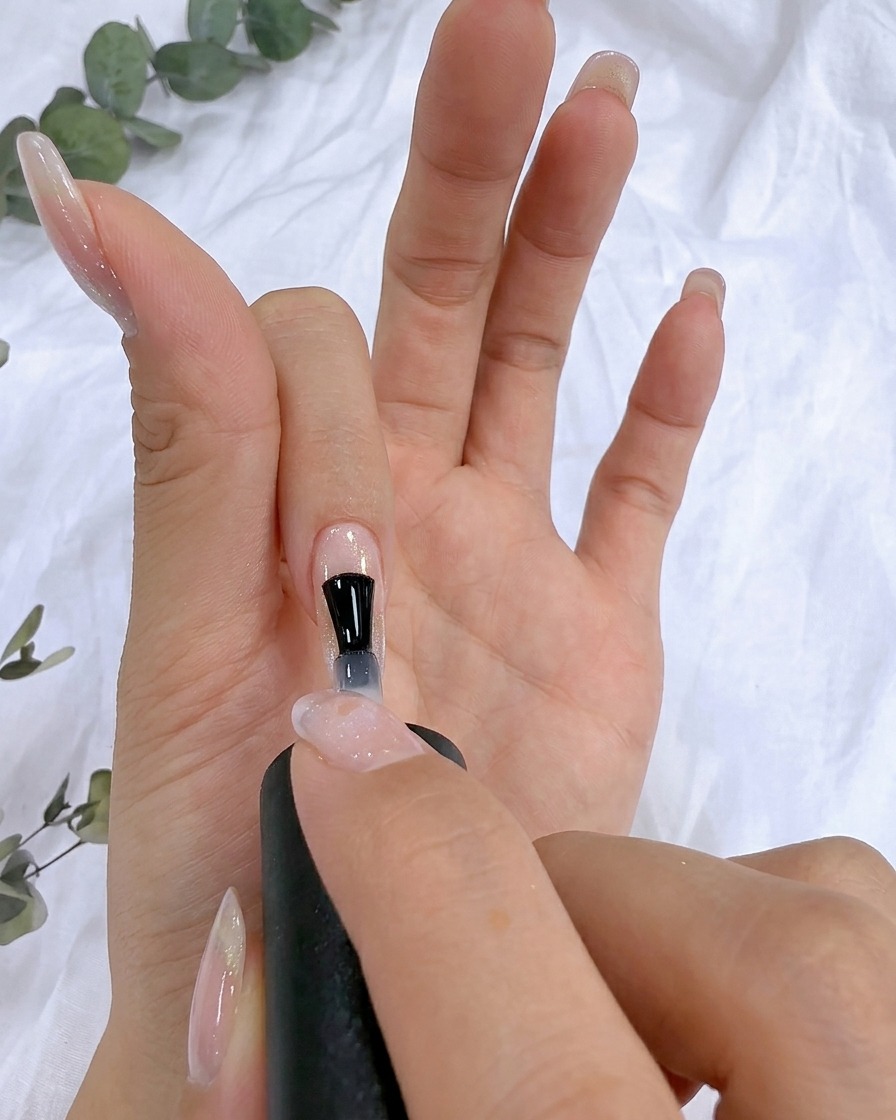 Un pinceau appliquant un gel renforçant transparent sur la surface dun ongle naturel.