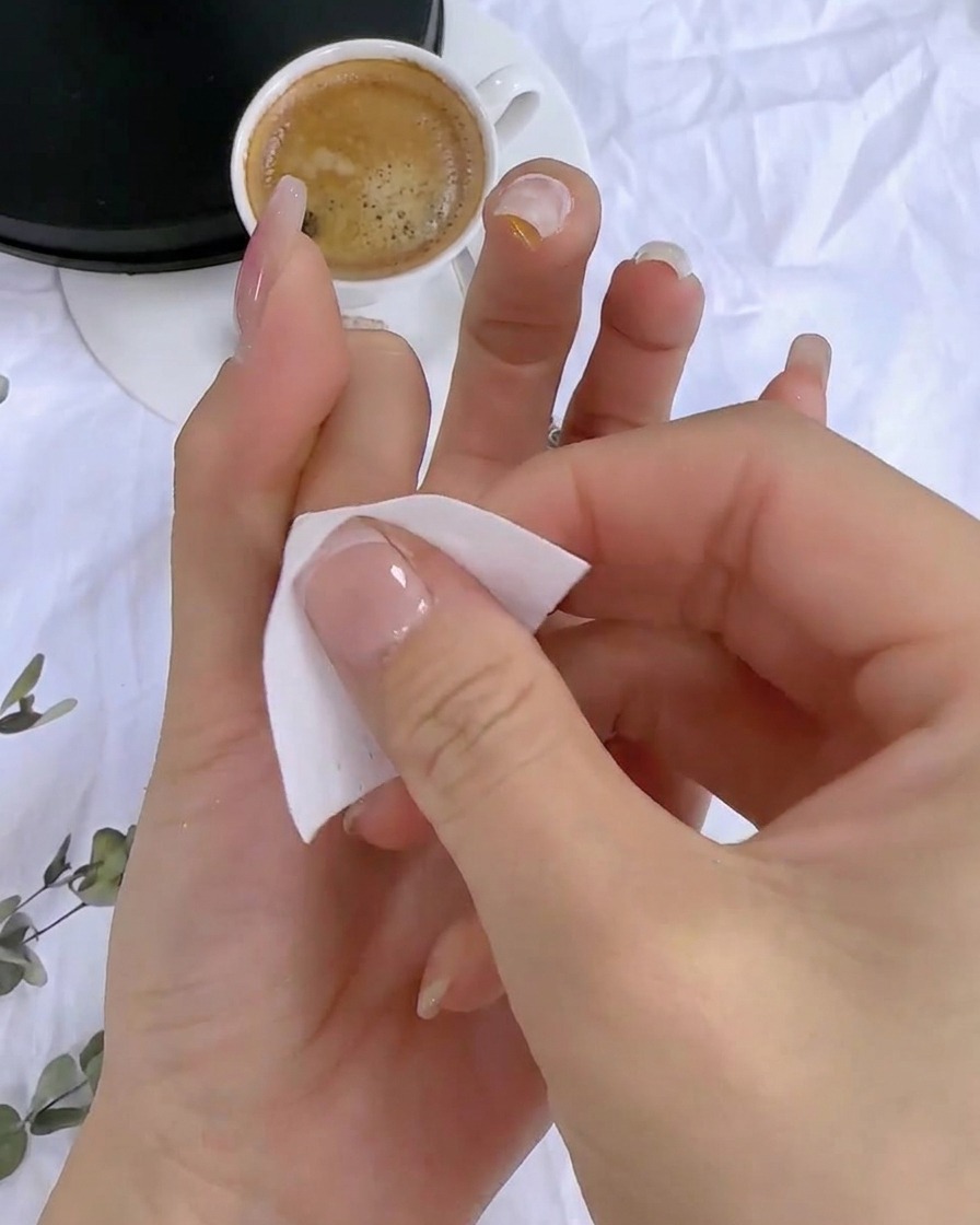 Une main utilisant une lingette non pelucheuse pour nettoyer le résidu collant sur la surface dun ongle catalysé.